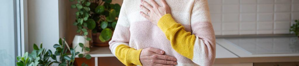 Femme ressentant des douleurs digestives avec les mains sur le ventre et la poitrine illustrant le lien entre stress et troubles intestinaux