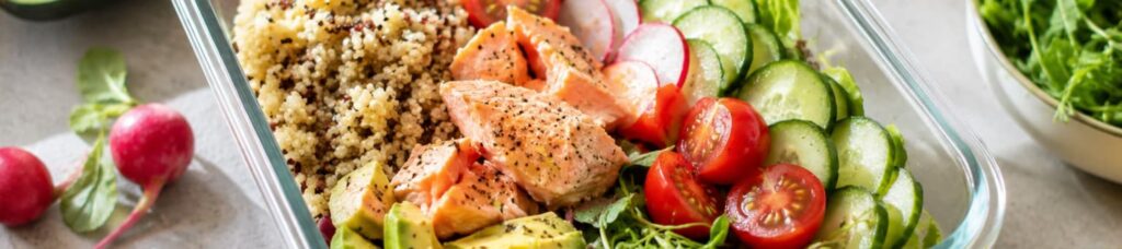 A balanced salad featuring salmon, avocado, quinoa, cucumber, cherry tomatoes, radishes, and microgreens served in a glass bowl—perfect for a healthy, nutrient-rich meal.